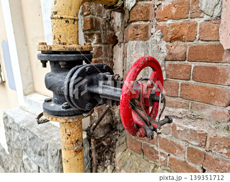 A vintage industrial gas valve is fixed to a rustic brick wall. The valve features a red handwheel that stands out against the worn bricks. This setup shows a blend of history and industrial design. A vintage industrial gas valve is fixed to a rustic brick wall. The valve features a red handwheel that stands out against the worn bricks. This setup shows a blend of history and industrial design. 139351712