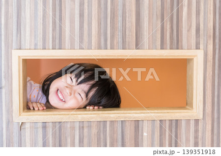キッズルームの木枠の穴から満面の笑みでのぞく日本人の女の子の幼児 キッズルームの木枠の穴から満面の笑みでのぞく日本人の女の子の幼児 139351918