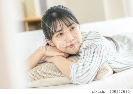 リビングで寝転んでくつろぐ眼鏡の若い女性 リビングで寝転んでくつろぐ眼鏡の若い女性 139352659