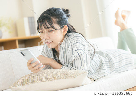 寝転んでスマホを見る眼鏡の女性 寝転んでスマホを見る眼鏡の女性 139352660