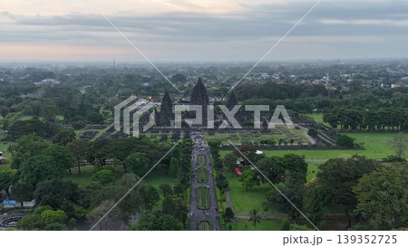 An enchanting evening aerial shot of the Prambanan Hindu Temple complex in Indonesia, featuring its iconic towering stone spires illuminated against a misty twilight sky and a sprawling cityscape. An enchanting evening aerial shot of the Prambanan Hindu Temple complex in Indonesia, featuring its iconic towering stone spires illuminated against a misty twilight sky and a sprawling cityscape. 139352725