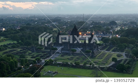 An enchanting evening aerial shot of the Prambanan Hindu Temple complex in Indonesia, featuring its iconic towering stone spires illuminated against a misty twilight sky and a sprawling cityscape. An enchanting evening aerial shot of the Prambanan Hindu Temple complex in Indonesia, featuring its iconic towering stone spires illuminated against a misty twilight sky and a sprawling cityscape. 139352729