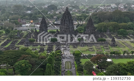 An enchanting evening aerial shot of the Prambanan Hindu Temple complex in Indonesia, featuring its iconic towering stone spires illuminated against a misty twilight sky and a sprawling cityscape. An enchanting evening aerial shot of the Prambanan Hindu Temple complex in Indonesia, featuring its iconic towering stone spires illuminated against a misty twilight sky and a sprawling cityscape. 139352730