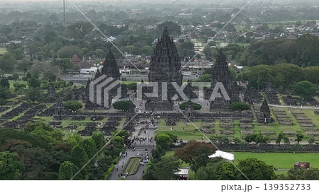 An enchanting evening aerial shot of the Prambanan Hindu Temple complex in Indonesia, featuring its iconic towering stone spires illuminated against a misty twilight sky and a sprawling cityscape. An enchanting evening aerial shot of the Prambanan Hindu Temple complex in Indonesia, featuring its iconic towering stone spires illuminated against a misty twilight sky and a sprawling cityscape. 139352733