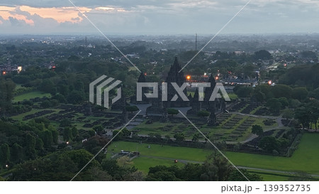 An enchanting evening aerial shot of the Prambanan Hindu Temple complex in Indonesia, featuring its iconic towering stone spires illuminated against a misty twilight sky and a sprawling cityscape. An enchanting evening aerial shot of the Prambanan Hindu Temple complex in Indonesia, featuring its iconic towering stone spires illuminated against a misty twilight sky and a sprawling cityscape. 139352735