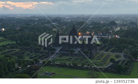 An enchanting evening aerial shot of the Prambanan Hindu Temple complex in Indonesia, featuring its iconic towering stone spires illuminated against a misty twilight sky and a sprawling cityscape. An enchanting evening aerial shot of the Prambanan Hindu Temple complex in Indonesia, featuring its iconic towering stone spires illuminated against a misty twilight sky and a sprawling cityscape. 139352736
