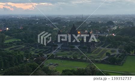 An enchanting evening aerial shot of the Prambanan Hindu Temple complex in Indonesia, featuring its iconic towering stone spires illuminated against a misty twilight sky and a sprawling cityscape. An enchanting evening aerial shot of the Prambanan Hindu Temple complex in Indonesia, featuring its iconic towering stone spires illuminated against a misty twilight sky and a sprawling cityscape. 139352737
