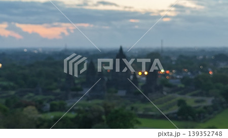 An enchanting evening aerial shot of the Prambanan Hindu Temple complex in Indonesia, featuring its iconic towering stone spires illuminated against a misty twilight sky and a sprawling cityscape. An enchanting evening aerial shot of the Prambanan Hindu Temple complex in Indonesia, featuring its iconic towering stone spires illuminated against a misty twilight sky and a sprawling cityscape. 139352748