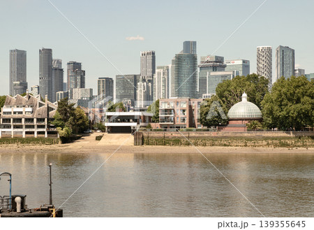 The composition of this image is grounded by the tranquil waters of the river in the foreground, leading the eye across a narrow sandy bank toward the distinctive glass-domed entrance of the Greenwich 139355645