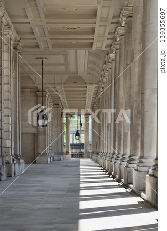 A rhythmic dance of light and shadow unfolds along this majestic colonnade at the Old Royal Naval College, where sunbeams pierce through towering pillars to cast a striking, geometric tapestry upon A rhythmic dance of light and shadow unfolds along this majestic colonnade at the Old Royal Naval College, where sunbeams pierce through towering pillars to cast a striking, geometric tapestry upon 139355697