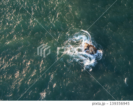Waves swirl around a rock in the ocean during daylight hours Waves swirl around a rock in the ocean during daylight hours 139356945
