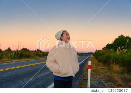Young asian woman in cozy coat smile on scenic roadside at dawn Young asian woman in cozy coat smile on scenic roadside at dawn 139358057