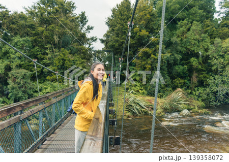Asian woman smiling on suspension bridge in lush forest at Lake Matheson, New Zealand 139358072
