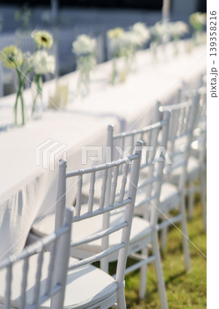 Elegant wedding long table with candle, white rose flower and white chairs in the garden 139358216