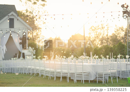 Elegant wedding long table with candle, white rose flower and white chairs in the garden Elegant wedding long table with candle, white rose flower and white chairs in the garden 139358225