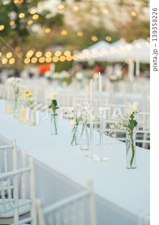 Elegant wedding long table with candle, white rose flower and white chairs in the garden 139358226