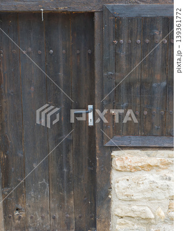 Old dark wooden door with a silver metal handle on a rustic stone building. Old dark wooden door with a silver metal handle on a rustic stone building. 139361772