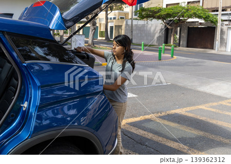 A teenager is standing in the back of a blue car 139362312