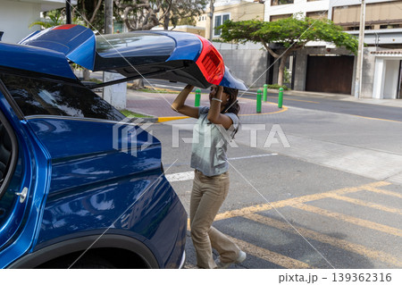A teenager is pulling out a bag from the back of a blue car A teenager is pulling out a bag from the back of a blue car 139362316