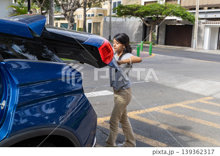 A teenager is pulling out the trunk of a blue car A teenager is pulling out the trunk of a blue car 139362317