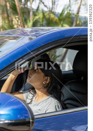 A teenager is looking at her reflection in the rear view mirror of a blue car A teenager is looking at her reflection in the rear view mirror of a blue car 139362320