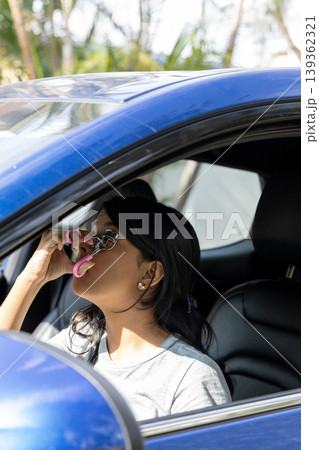 A teenager is driving a blue car and is using a pink phone A teenager is driving a blue car and is using a pink phone 139362321