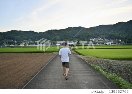 田園風景が広がる田舎道を歩く男性の後ろ姿 夏の帰省イメージ 139362762