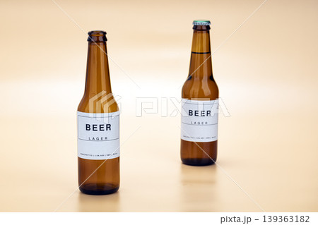 Two Handcrafted Small Batch Lager Beer Bottles in Amber Glass With Clean Minimalist White Labels Displayed on a Soft Warm Beige Studio Background Surface Two Handcrafted Small Batch Lager Beer Bottles in Amber Glass With Clean Minimalist White Labels Displayed on a Soft Warm Beige Studio Background Surface 139363182