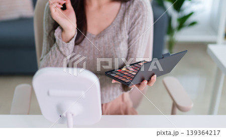 young Asian women holding makeup eyeshadow palette cosmetic product choosing color applying beauty routine sitting home interior living room table mirror soft young Asian women holding makeup eyeshadow palette cosmetic product choosing color applying beauty routine sitting home interior living room table mirror soft 139364217