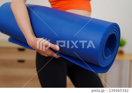woman holding blue yoga mat preparing for home workout fitness exercise training session indoor wellness activity healthy lifestyle concept ready for pilates 139365382