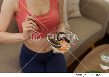 Asian women eating healthy fruit salad bowl with yogurt berries after workout exercise at home living room fitness wellness lifestyle nutrition diet weight Asian women eating healthy fruit salad bowl with yogurt berries after workout exercise at home living room fitness wellness lifestyle nutrition diet weight 139365389
