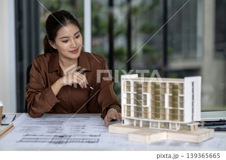 Asian adult woman architect designer reviewing building model plans developing urban design project focused professional work architectural studio Asian adult woman architect designer reviewing building model plans developing urban design project focused professional work architectural studio 139365665
