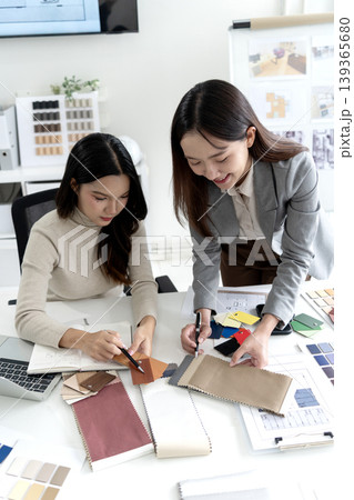 Asian adult women designers collaborate on interior project selecting fabric samples color palettes material swatches in modern office studio 139365680