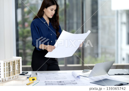 Asian Adult Woman Architect Engineer Reviewing Building Construction Blueprints Design Plans Project Development Office Workspace Asian Adult Woman Architect Engineer Reviewing Building Construction Blueprints Design Plans Project Development Office Workspace 139365742