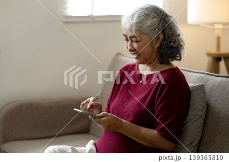 Older Asian Adult Woman Happily Uses Smartphone Browsing Internet Home Sofa Living Room Relaxing Modern Technology Communication Lifestyle 139365810