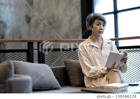 Adult Asian woman relaxing reading book in modern contemporary lounge cafe interior for thoughtful quiet moment 139366124