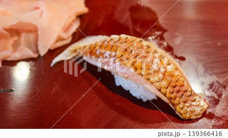 close up of a Japanese sushi with raw akamutsu Sushi with seared fish slice on rice, golden-brown skin, and pickled ginger on glossy red surface with copy space 139366416