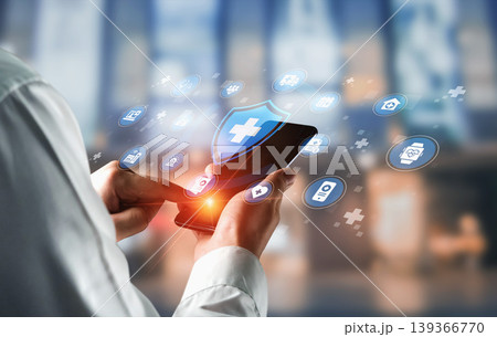 Hands Using Mobile Device With Health Icons And Security Shield Symbolizing Digital Health Technology And Medical Services In Modern Urban Setting Ledger Hands Using Mobile Device With Health Icons And Security Shield Symbolizing Digital Health Technology And Medical Services In Modern Urban Setting Ledger 139366770