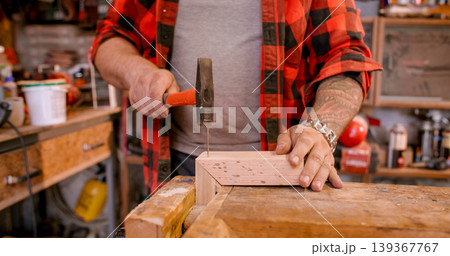 Joinery process. Woodworking hand tool. Male carpenter hand hammering nail into frame corner. Professional occupation at workbench. 139367767