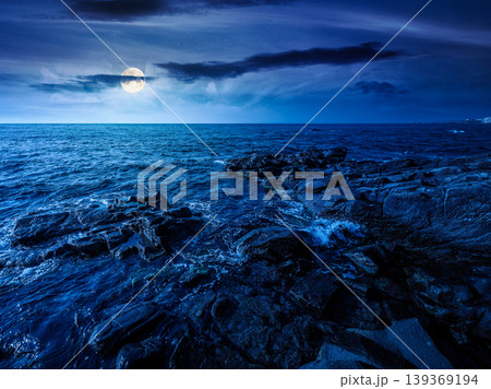sea coast with stones and boulders at night. view of beach with rock in seaweed. full moon over dynamic cloudscape on the sky above horizon. mysterious summer vacations background concept 139369194