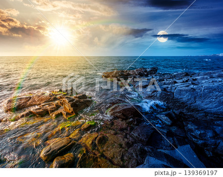 day meet night. sea coast with stones and boulders. view of beach with rock in seaweed. sun and moon on epic sky above horizon. autumn equinox harmony concept for astrology background 139369197