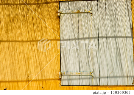 Shadows and light create lines on a yellow wall with a shutter on window in a sunny outdoor setting Shadows and light create lines on a yellow wall with a shutter on window in a sunny outdoor setting 139369365