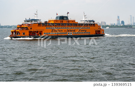 New york, usa august 16,2024. Iconic orange staten island ferry crossing new york harbor with passengers and the manhattan skyline on a cloudy summer day New york, usa august 16,2024. Iconic orange staten island ferry crossing new york harbor with passengers and the manhattan skyline on a cloudy summer day 139369515