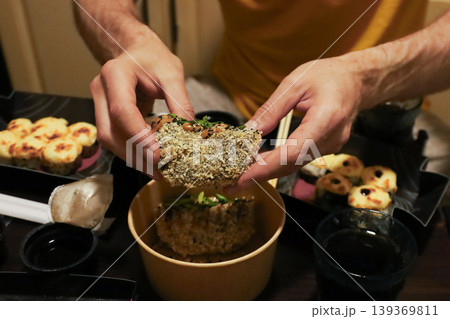 Hands holding a specialty sushi roll with crispy coating and creamy sauce during a meal 139369811