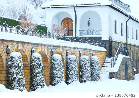 A serene winter scene unfolds as fresh snow covers the grounds and architecture of a venerable monastery building nestled within a historical area A serene winter scene unfolds as fresh snow covers the grounds and architecture of a venerable monastery building nestled within a historical area 139370482