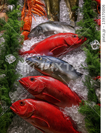 Red and silver fish rest on crushed ice at a seafood market display. Bright colors and ice-covered fish attract shoppers. 139370806