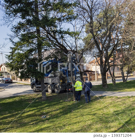 Nitra, Slovakia - March 12, 2026: Two workers in transparent orange protective clothing perform underground maintenance through an open manhole. A vacuum sewer service truck is located outside. 139371204