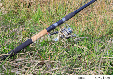 Fishing rod with spinning reel on green grass Fishing rod with spinning reel on green grass 139371286