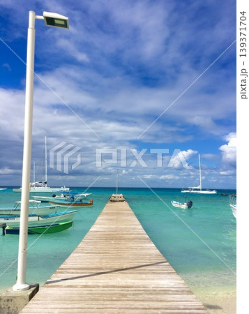 Bright tropical sea with wooden pier and boats under blue sky, summer travel destination background Bright tropical sea with wooden pier and boats under blue sky, summer travel destination background 139371704