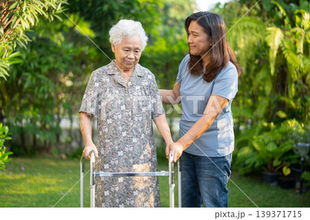 Caregiver help Asian elderly woman patient walk with walker in park. 139371715
